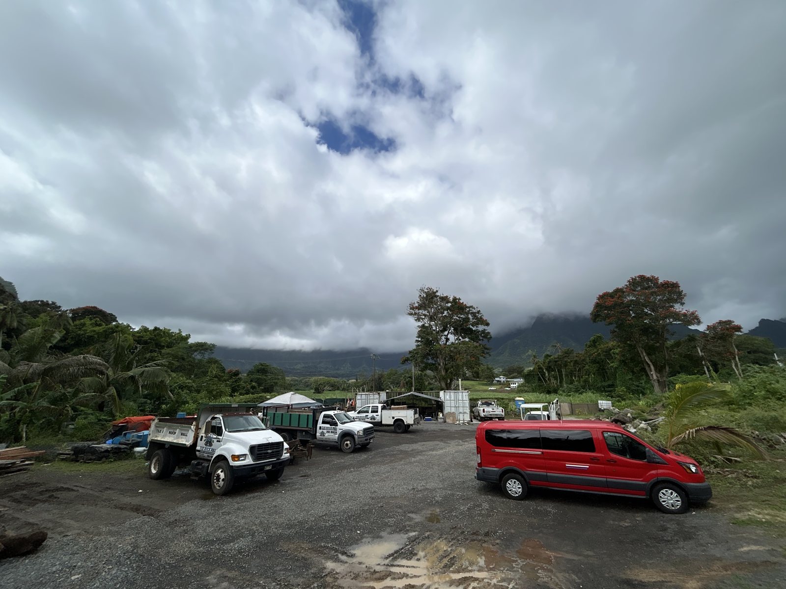Work vehicles in an outdoor yard with mountains and cloudy sky in the distance